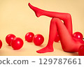 Long slim woman legs in red tights lying on beige background among red balloons 129787661