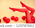 Long slim woman legs in red tights lying on beige background among red balloons 129787662