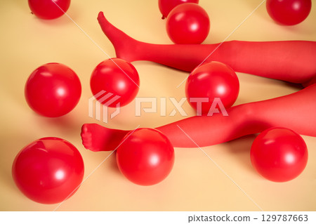 Long slim woman legs in red tights lying on beige background among red balloons Long slim woman legs in red tights lying on beige background among red balloons 129787663