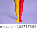 Long slim woman legs in multicolor yellow and red tights against purple background. 129787664