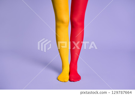 Long slim woman legs in multicolor yellow and red tights against purple background. Long slim woman legs in multicolor yellow and red tights against purple background. 129787664