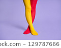 Long slim woman legs in multicolor yellow and red tights against purple background. 129787666