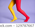 Long slim woman legs in multicolor yellow and red tights against purple background. 129787667