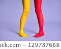Long slim woman legs in multicolor yellow and red tights against purple background. 129787668