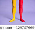 Long slim woman legs in multicolor yellow and red tights against purple background. 129787669
