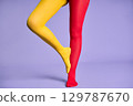 Long slim woman legs in multicolor yellow and red tights against purple background. 129787670