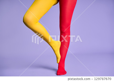 Long slim woman legs in multicolor yellow and red tights against purple background. 129787670