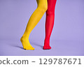 Long slim woman legs in multicolor yellow and red tights against purple background. 129787671