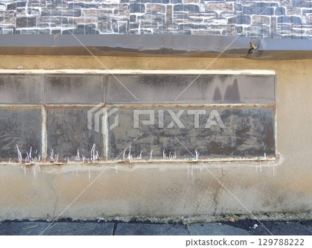 gray facade of old building with large closed window, paint drips and rust on metal parts, architectural retro background with fragment of outbuilding gray facade of old building with large closed window, paint drips and rust on metal parts, architectural retro background with fragment of outbuilding 129788222