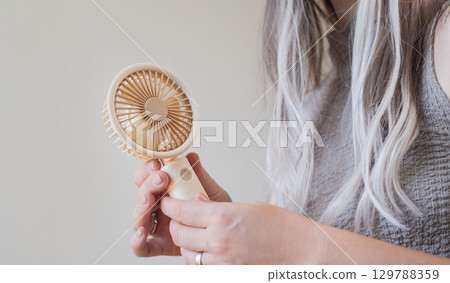 Happy young woman cooling off with her personal fan outdoors on a bright warm sunny day in summer. 129788359