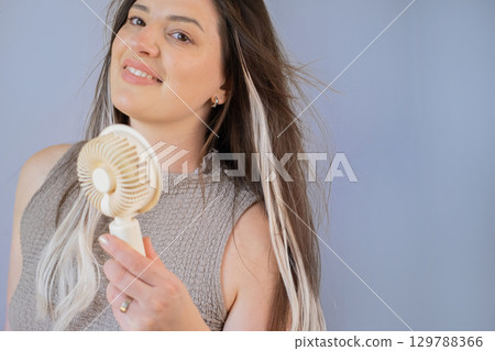 Young woman holding a compact fan feeling refreshed and cool outdoors on a hot sunny summer day. Young woman holding a compact fan feeling refreshed and cool outdoors on a hot sunny summer day. 129788366