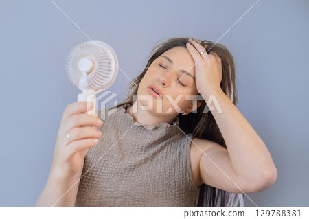 Young woman enjoying cool air from a mini fan outdoors on a hot sunny summer day. 129788381
