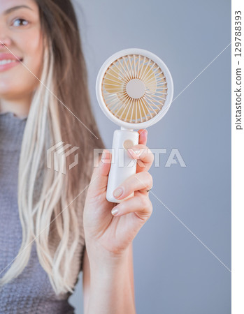 Young woman enjoying cool air from her personal mini fan on a warm sunny day outdoors. Young woman enjoying cool air from her personal mini fan on a warm sunny day outdoors. 129788393