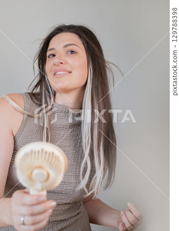 Young woman enjoying a handheld mini fan staying cool and stylish outdoors on a hot sunny summer day. 129788398
