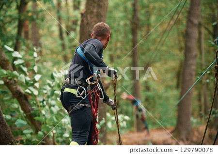 Process of preparing. Man is doing climbing in the forest by use of safety equipment Process of preparing. Man is doing climbing in the forest by use of safety equipment 129790078