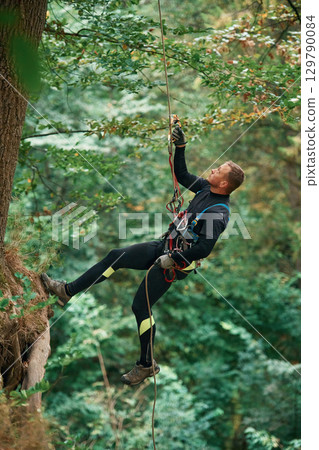 Hanging on a rope. Man is doing climbing in the forest by use of safety equipment 129790084