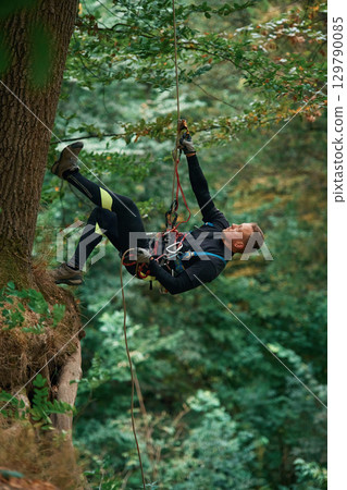 Hanging on a rope. Man is doing climbing in the forest by use of safety equipment Hanging on a rope. Man is doing climbing in the forest by use of safety equipment 129790085
