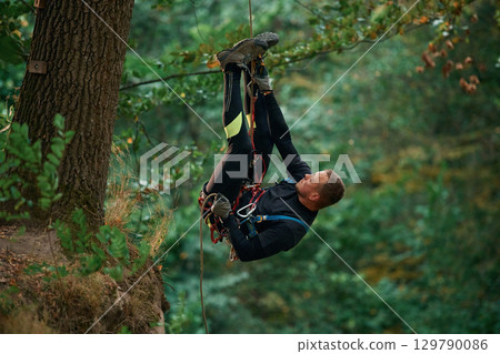 Hanging on a rope. Man is doing climbing in the forest by use of safety equipment Hanging on a rope. Man is doing climbing in the forest by use of safety equipment 129790086