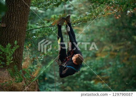 Up on the rope, hanging. Man is doing climbing in the forest by use of safety equipment 129790087