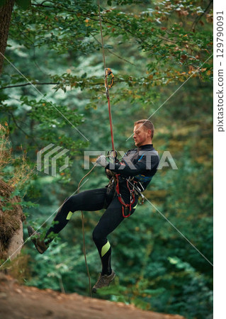 Up on the rope, hanging. Man is doing climbing in the forest by use of safety equipment 129790091