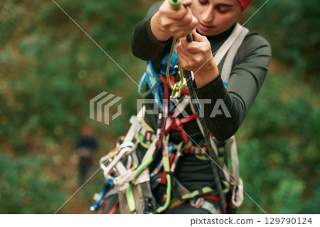 Front view. Woman is doing climbing in the forest by the use of safety equipment 129790124
