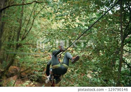 Climbing in the forest. Woman is in the forest using the safety equipment Climbing in the forest. Woman is in the forest using the safety equipment 129790146