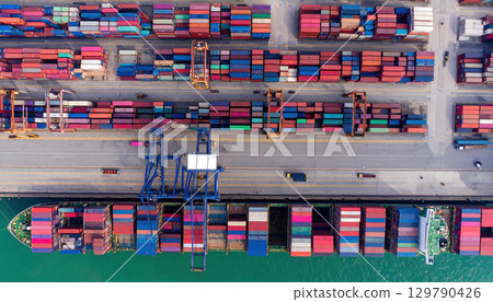 Aerial view of busy shipping port with colorful containers stacked along dock and cargo ship docked, showcasing industrial activity and maritime logistics 129790426