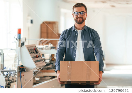 In the glasses. Handsome man is working at the factory of creating eco boxes In the glasses. Handsome man is working at the factory of creating eco boxes 129790651