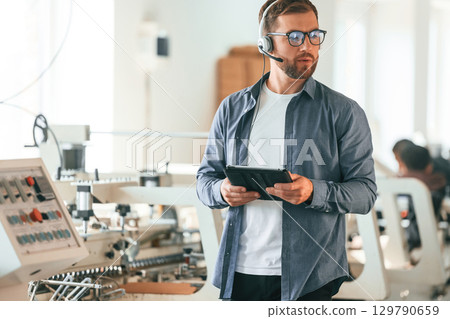 With tablet in hands. Handsome man is working at the factory of creating eco boxes 129790659
