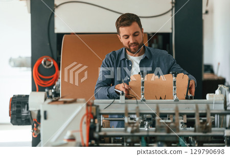 Cardboards in hands. Handsome man is working at the factory of creating eco boxes 129790698