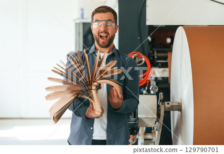 With raw material, paper. Handsome man is working at the factory of creating eco boxes With raw material, paper. Handsome man is working at the factory of creating eco boxes 129790701
