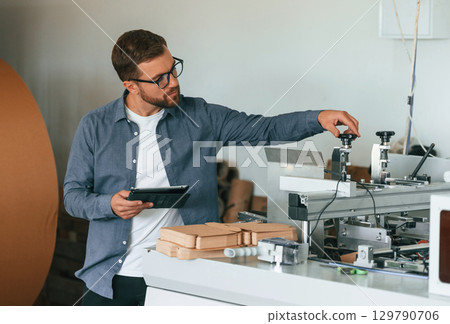 Front view. Handsome man is working at the factory of creating eco boxes Front view. Handsome man is working at the factory of creating eco boxes 129790706