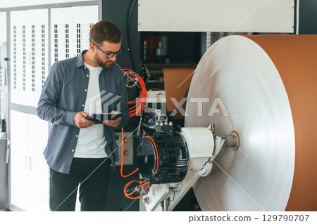 By the rounded machine for making paper. Handsome man is working at the factory of creating eco boxes By the rounded machine for making paper. Handsome man is working at the factory of creating eco boxes 129790707