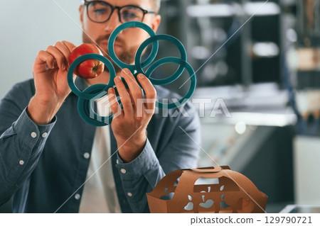 With an apple. Handsome man is working at the factory of creating eco boxes 129790721