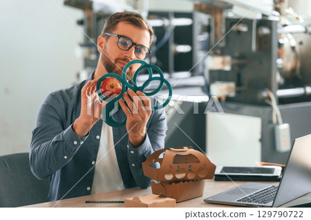 Sitting by the table. Handsome man is working at the factory of creating eco boxes 129790722