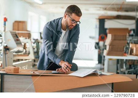 Document on the table. Handsome man is working at the factory of creating eco boxes 129790728