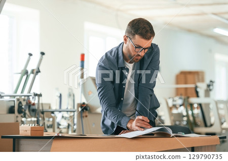 Table, document on it. Handsome man is working at the factory of creating eco boxes 129790735