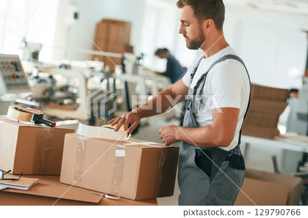 White shirt and grey uniform. Handsome man is working at the factory of creating eco boxes White shirt and grey uniform. Handsome man is working at the factory of creating eco boxes 129790766