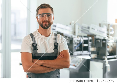Standing with arms crossed. Handsome man is working at the factory of creating eco boxes Standing with arms crossed. Handsome man is working at the factory of creating eco boxes 129790779