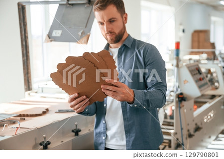 Looking at cardboards. Handsome man is working at the factory of creating eco boxes 129790801