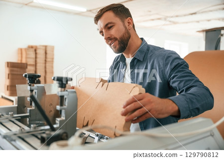 Raw material, bunch of cardboards. Handsome man is working at the factory of creating eco boxes 129790812