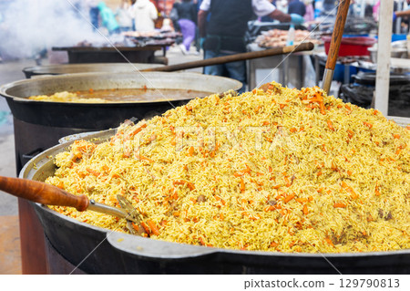 A large cauldron with a huge pile of traditional pilaf at a bustling outdoor street food festival. 129790813
