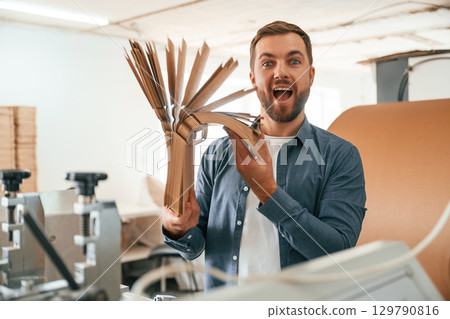 Bunch of cardboards in hands. Handsome man is working at the factory of creating eco boxes 129790816