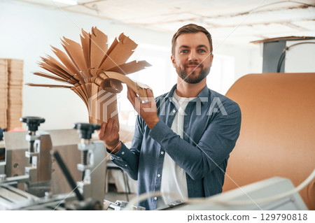 Bunch of cardboards in hands. Handsome man is working at the factory of creating eco boxes 129790818