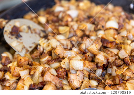 A close-up of a large pan filled with sizzling fried pork and onion, a delicious and rustic meal. A close-up of a large pan filled with sizzling fried pork and onion, a delicious and rustic meal. 129790819