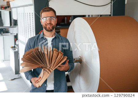Many of the cardboards in hands. Handsome man is working at the factory of creating eco boxes Many of the cardboards in hands. Handsome man is working at the factory of creating eco boxes 129790824