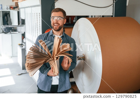Many of the cardboards in hands. Handsome man is working at the factory of creating eco boxes Many of the cardboards in hands. Handsome man is working at the factory of creating eco boxes 129790825