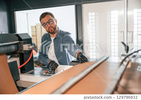 By the machine. Handsome man is working at the factory of creating eco boxes 129790832