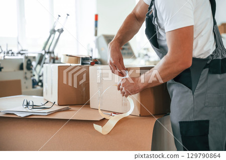 Process of packaging the product. Handsome man is working at the factory of creating eco boxes Process of packaging the product. Handsome man is working at the factory of creating eco boxes 129790864