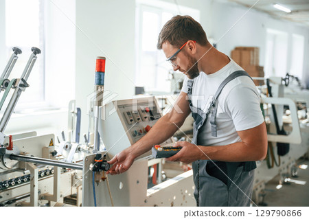 Standing by the machine. Handsome man is working at the factory of creating eco boxes 129790866